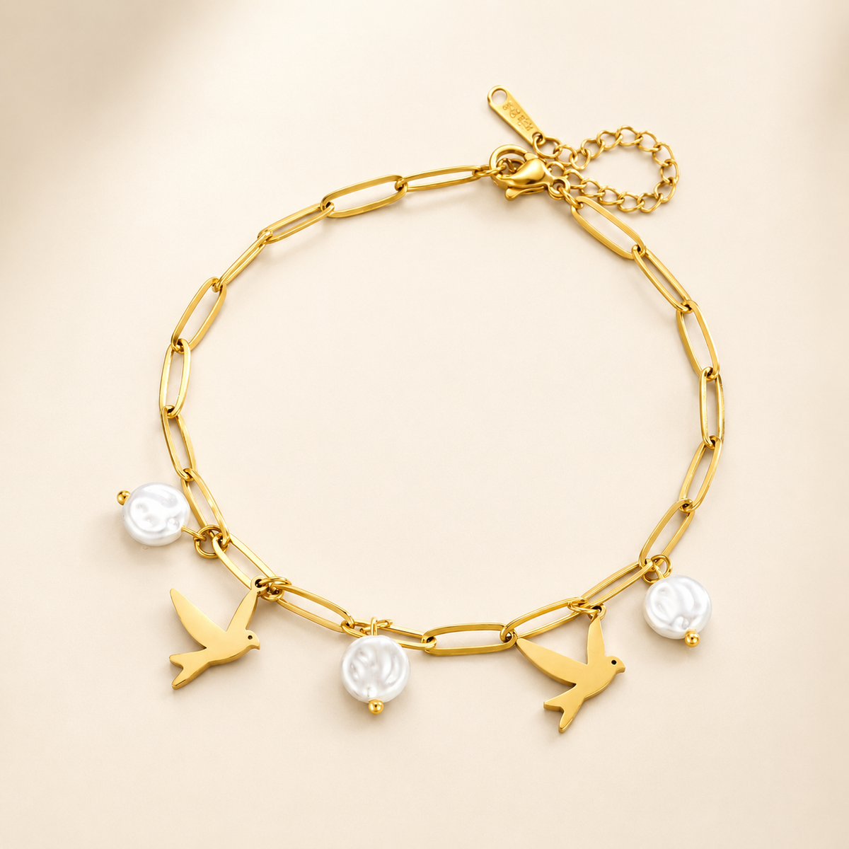Gold paperclip anklet with two swallow charms and three coin pearls on luxury ivory background