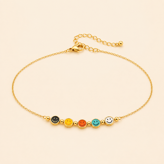 Gold anklet with five colourful enamel smiley face charms on a warm ivory background