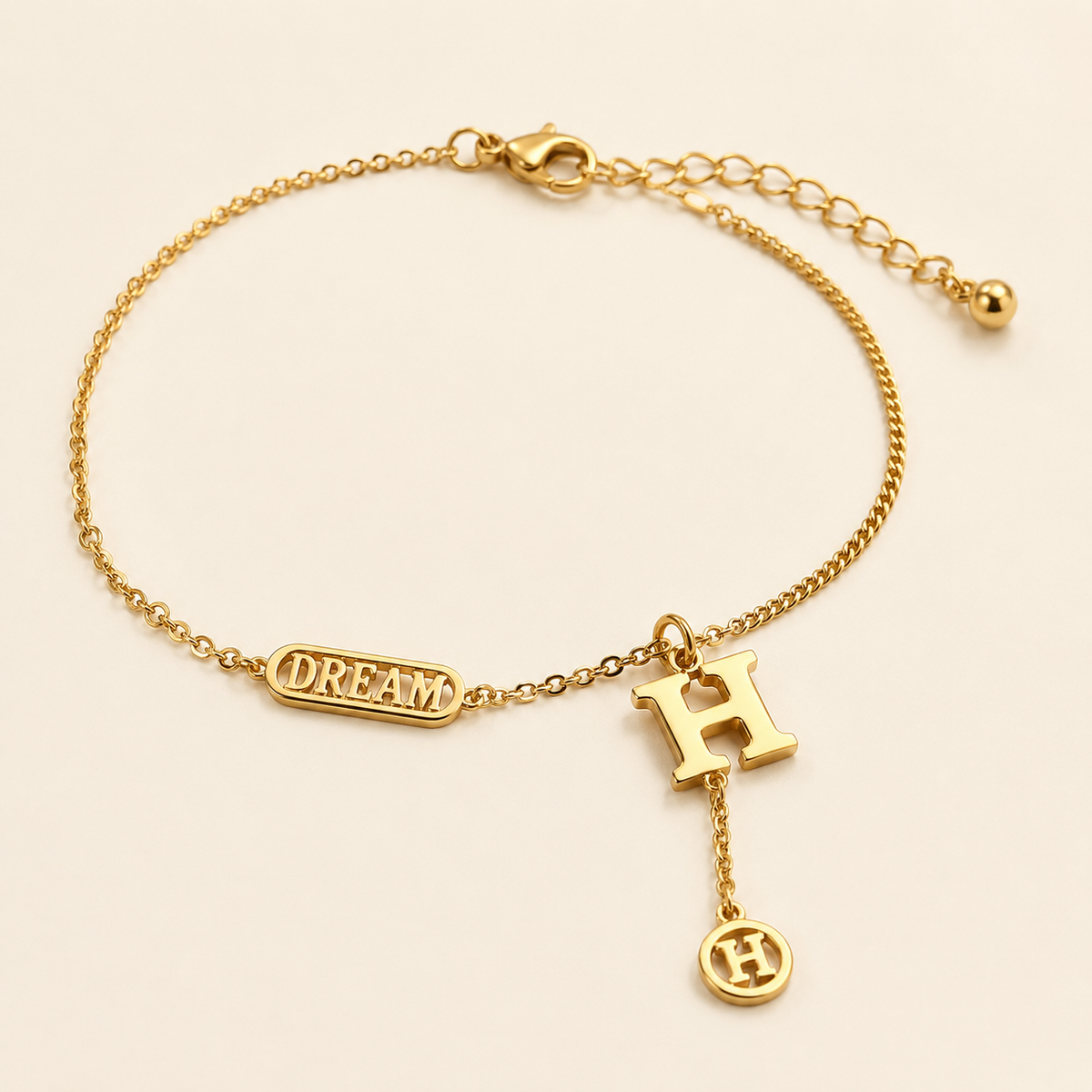 Gold letter H anklet with DREAM plaque and H medallion tassel on warm ivory