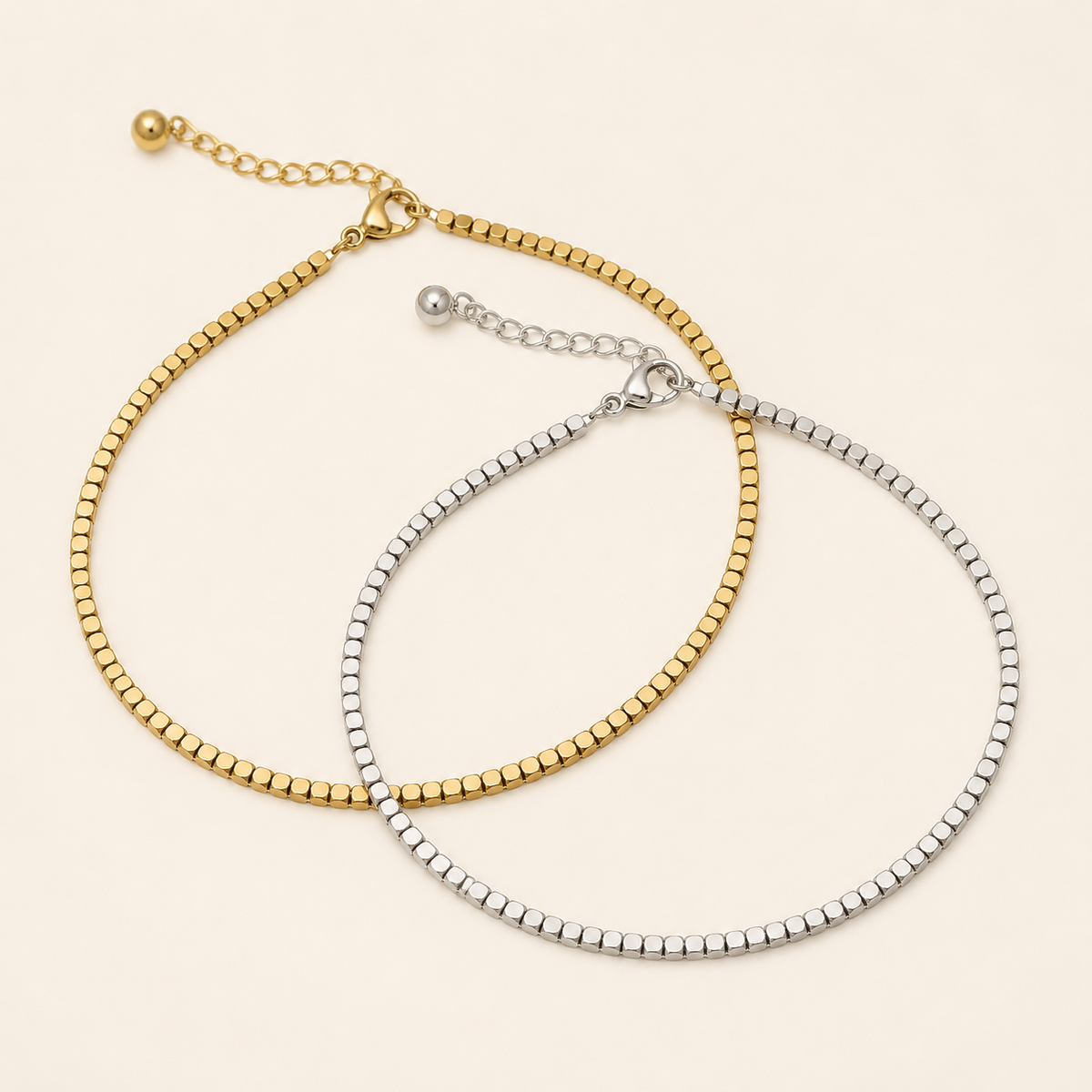 Matching gold and silver faceted chain anklets on a warm ivory background